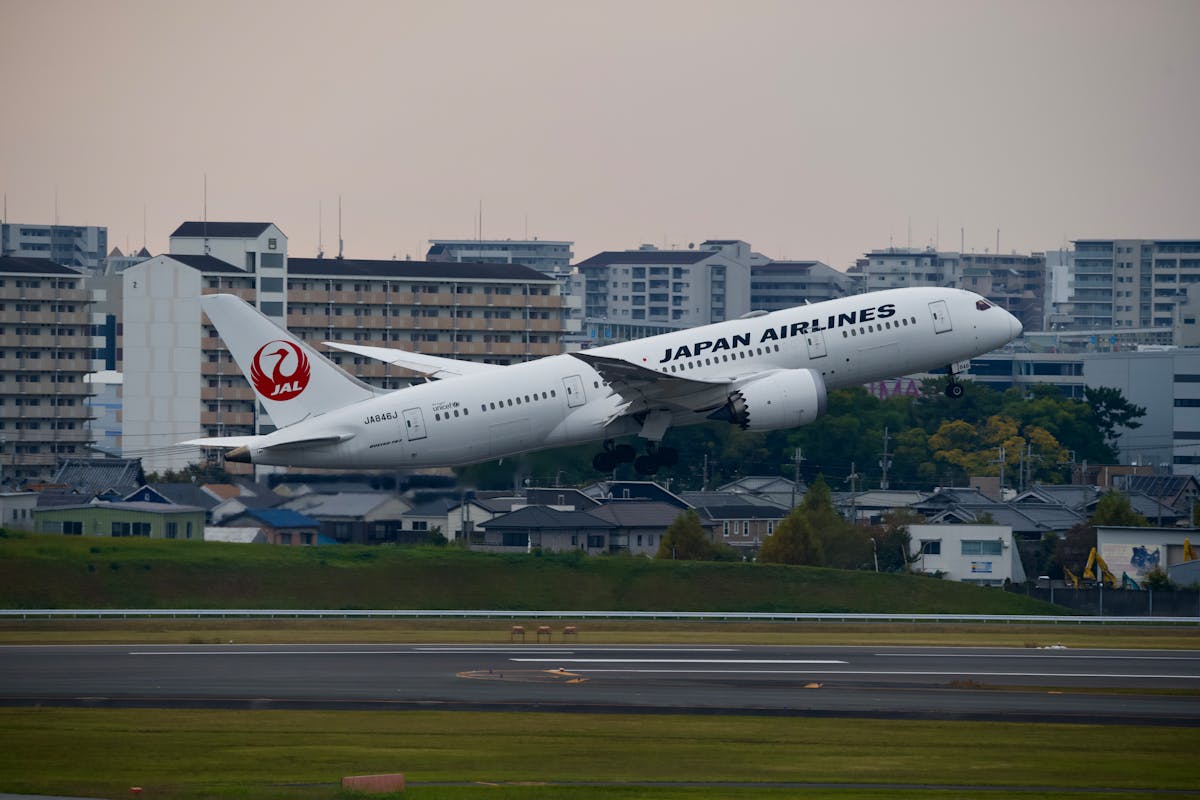 Japan Airlines Boeing 787 taking off at Tokyo urban airport with city skyline in background