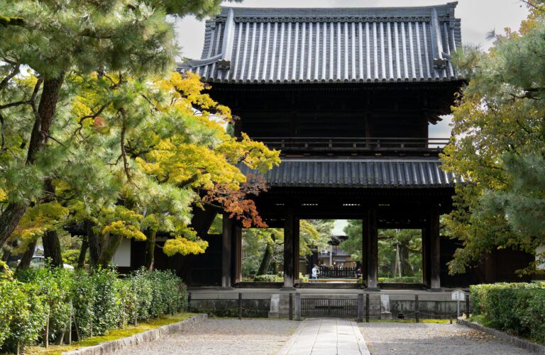 Traditional Japanese temple gate framed by vibrant autumn foliage in a rural setting