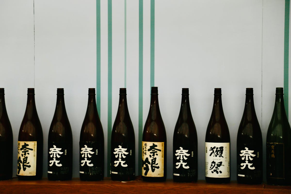 Row of traditional Japanese sake bottles with distinctive labels on a wooden shelf