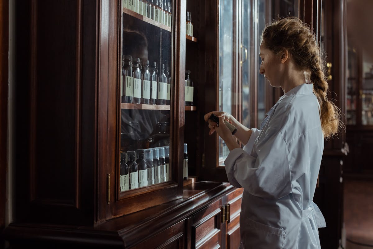 Female pharmacist in white uniform organizing prescription bottles in pharmacy cabinet